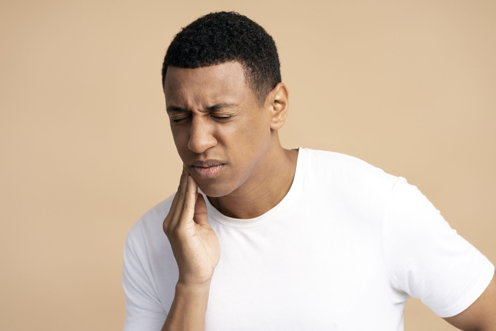 Dental problems. Portrait of unhealthy man pressing sore cheek, suffering acute toothache, periodontal disease, cavities or jaw pain. Indoor studio shot isolated on beige background